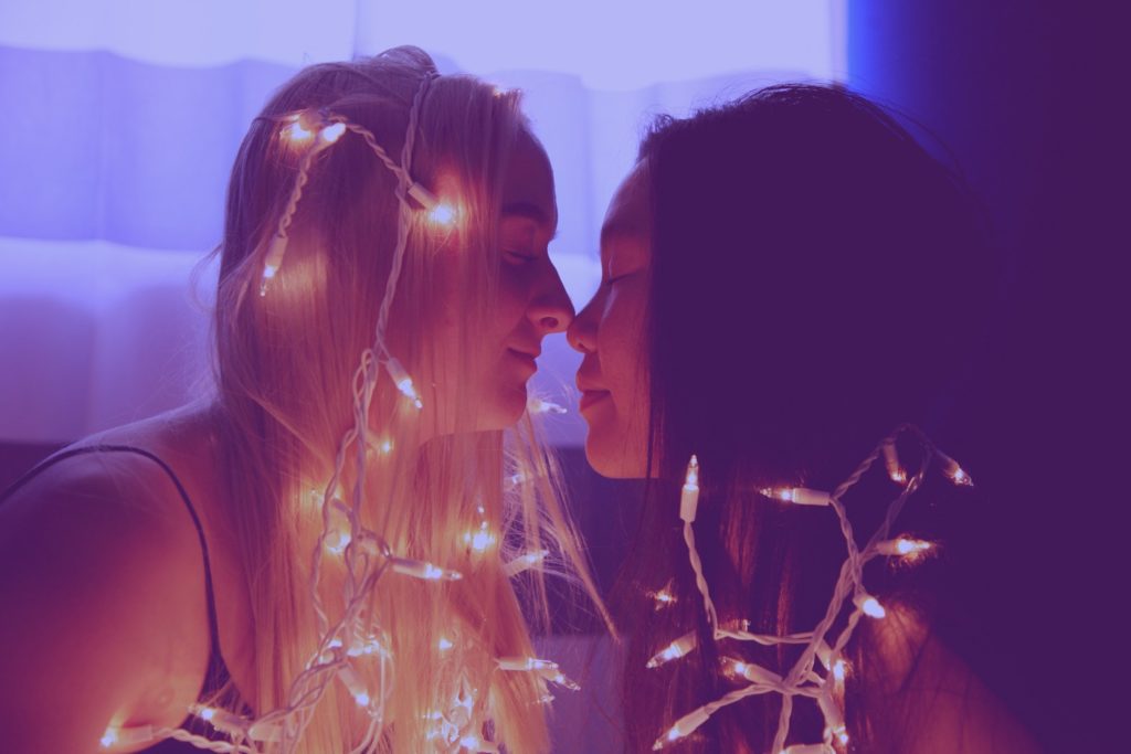 A interracial lesbian couple flirting with each other in the dark, with fairy lights surrounded their body